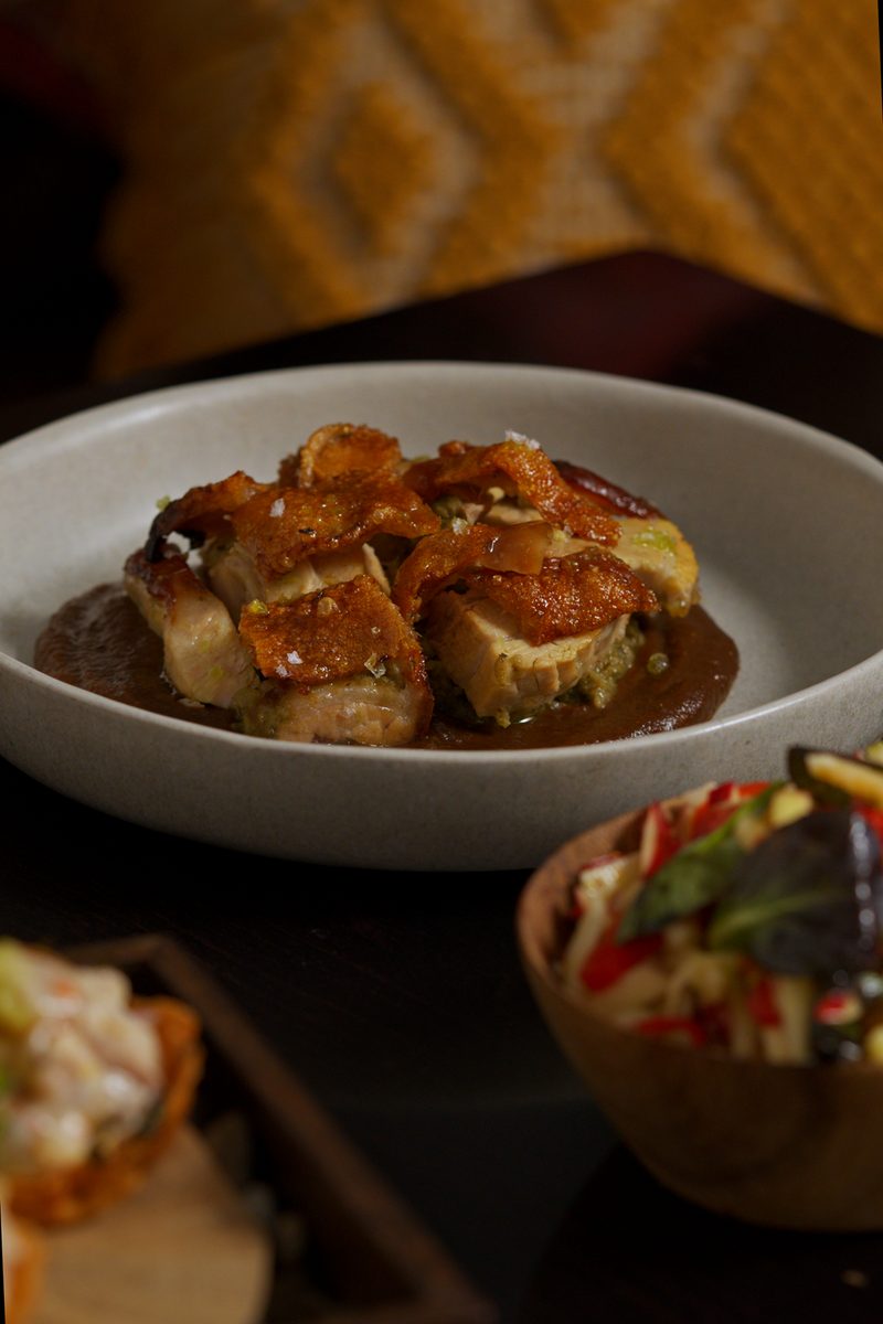 Crispy pork belly lechon, sliced over a dark sauce in a grey bowl, at Nanam in Takapuna