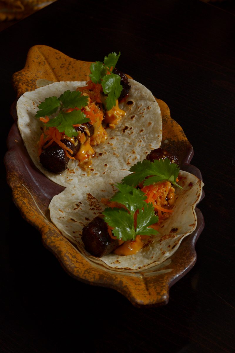 Two Wagyu longganisa tacos topped with shredded carrot, sauce and fresh coriander on a leaf shaped plate at Nanam in Takapuna